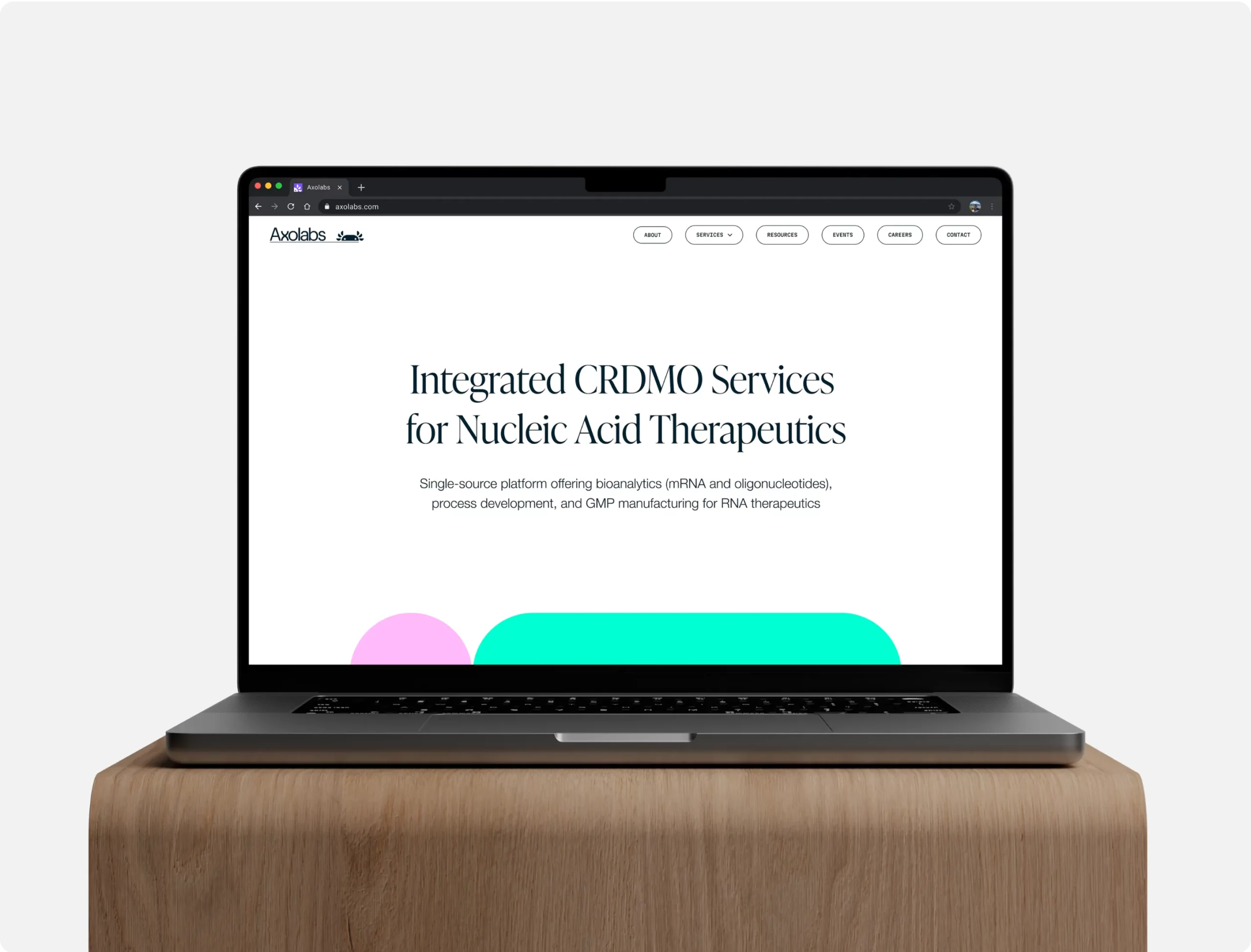 A laptop on a wooden surface displays the Axolabs homepage with a headline about CRDMO services for nucleic acid therapeutics and a clean, minimal design.